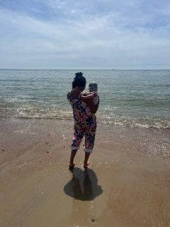 Woman holding a baby on the beach gazing the sea on a sunny day